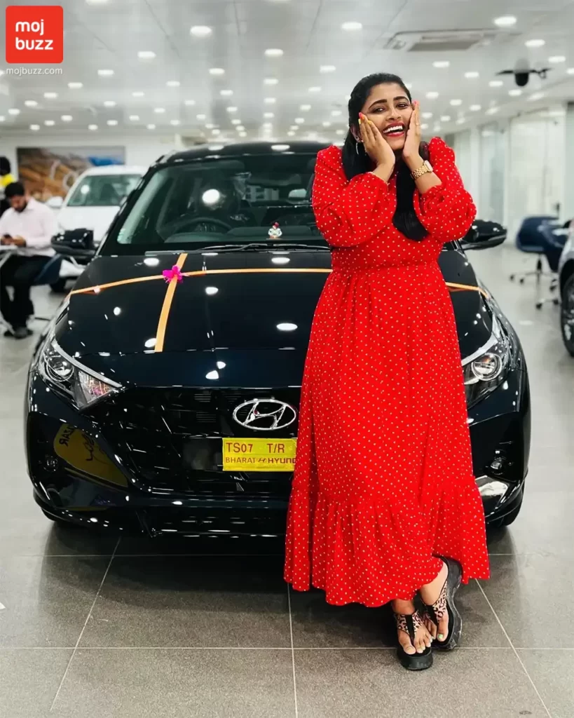 A girl (Geetu Royal) standing in front of a new car feeling happy