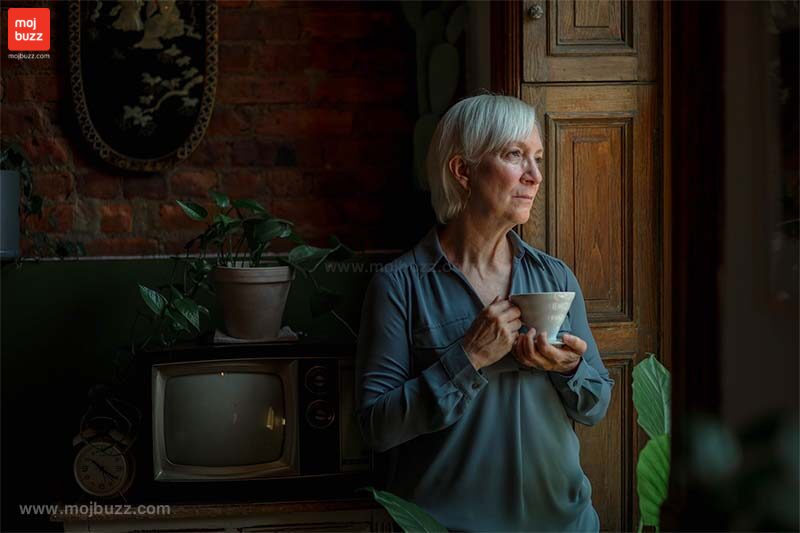 An older women having tea or coffee and standing on the door alone